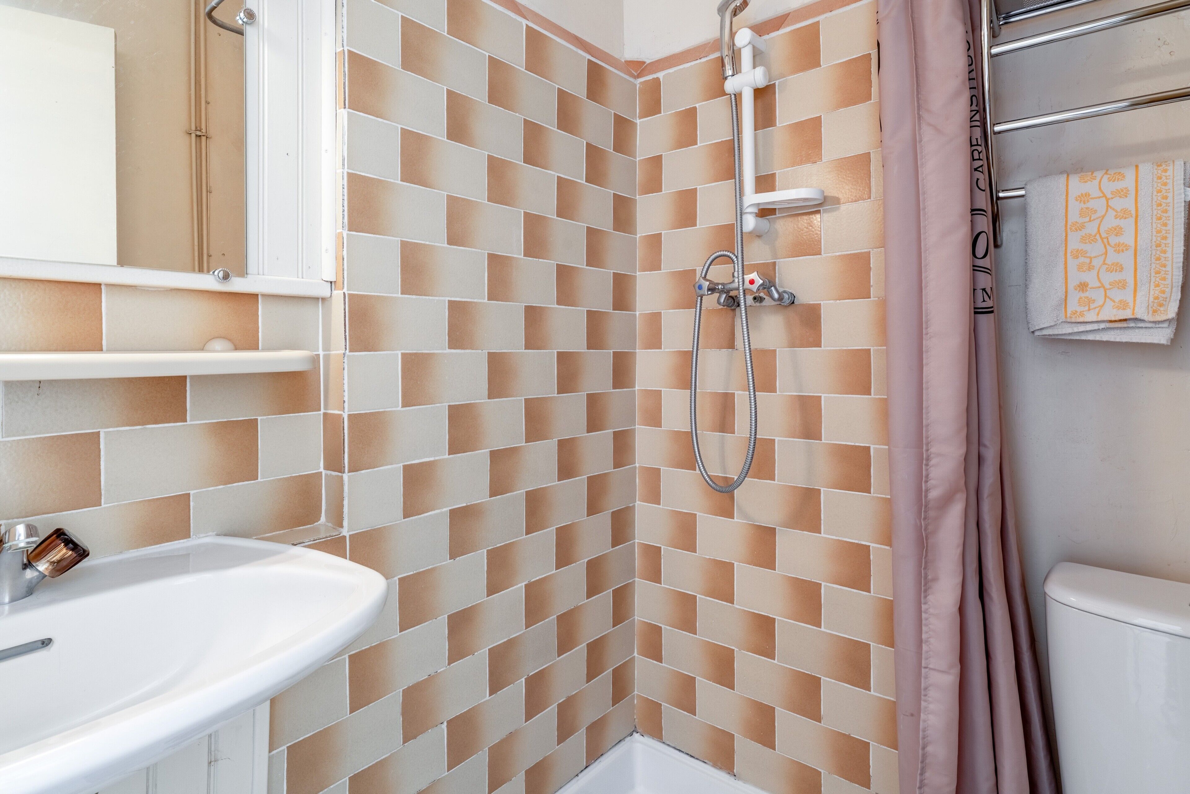 Een badkamer met betegelde douchewand, een wastafel en een toilet.