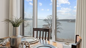 Ein Essbereich mit einem Tisch für zwei Personen, einer Pflanze in einer Vase und Seeblick durch große Fenster.