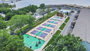 Ein mehrstöckiges Hotel mit Tennisplatz, Schwimmbad und Blick auf einen Fluss und eine Brücke.