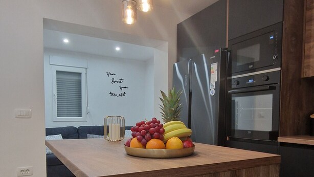 Una cucina moderna con isola in legno, elettrodomestici in acciaio inossidabile e una ciotola di frutta sull'isola.