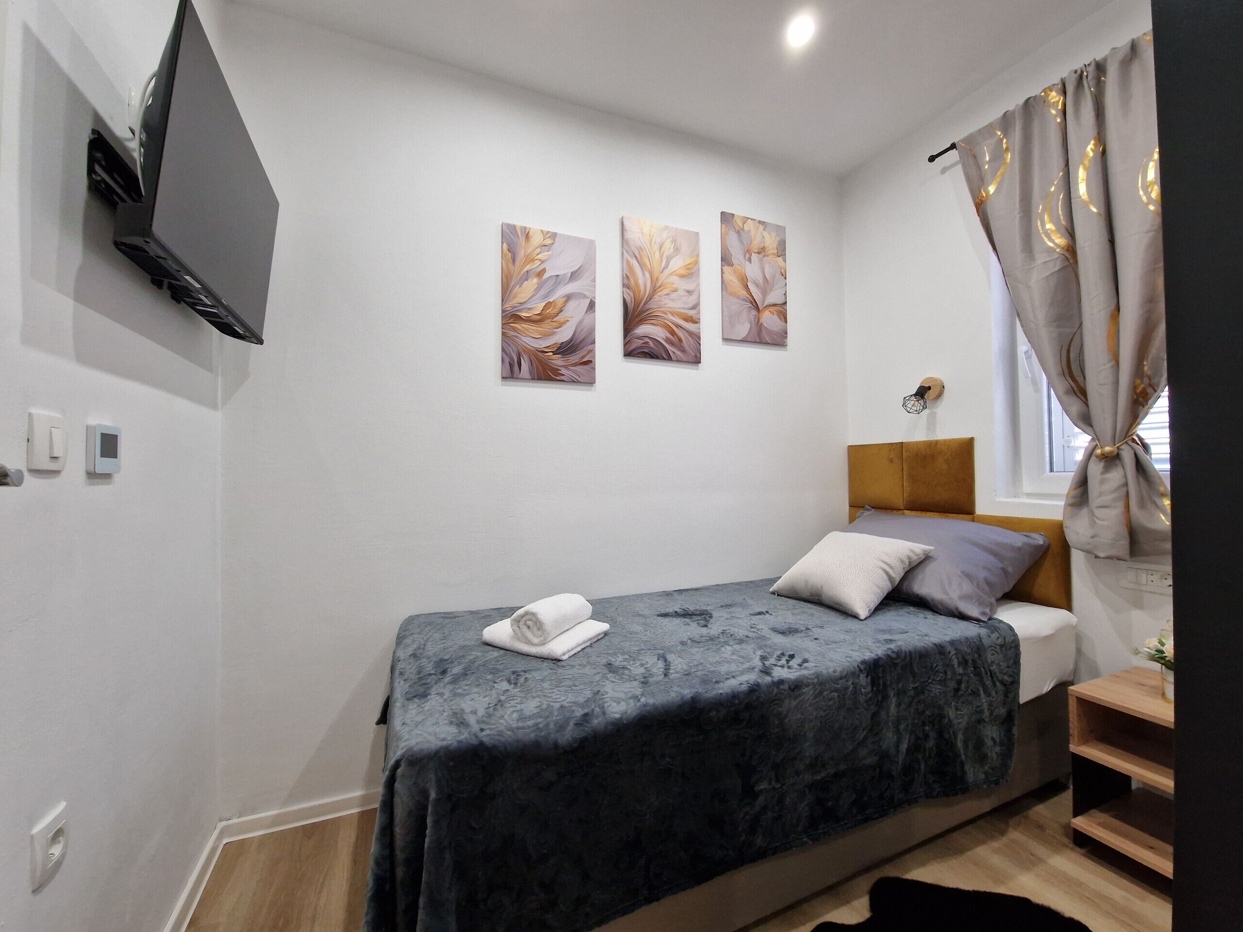 A bedroom with a bed, a flat-screen TV mounted on the wall, and three wall-mounted paintings.