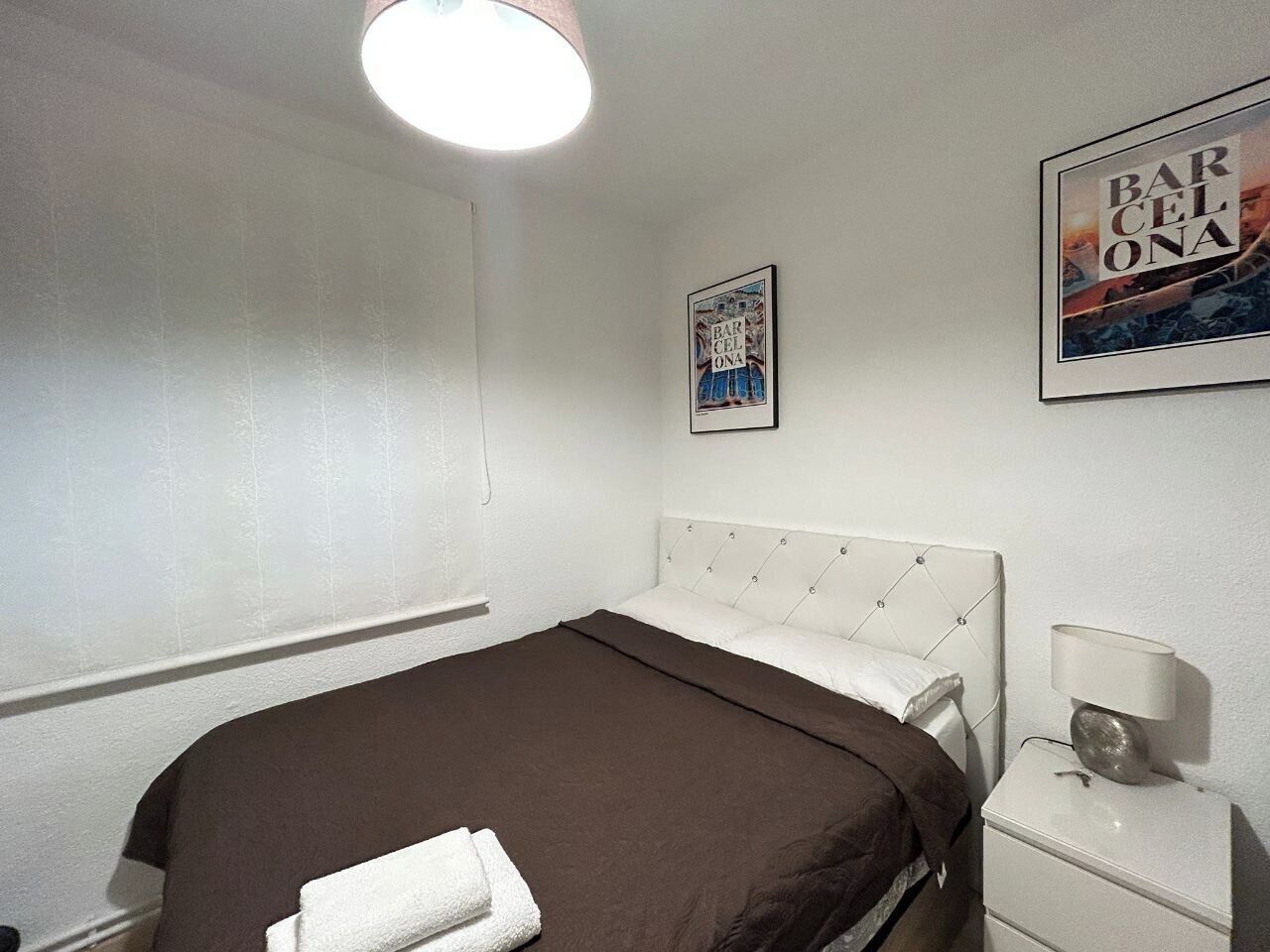 Un dormitorio con cama, mesita de noche, lámpara y dos cuadros en la pared.
