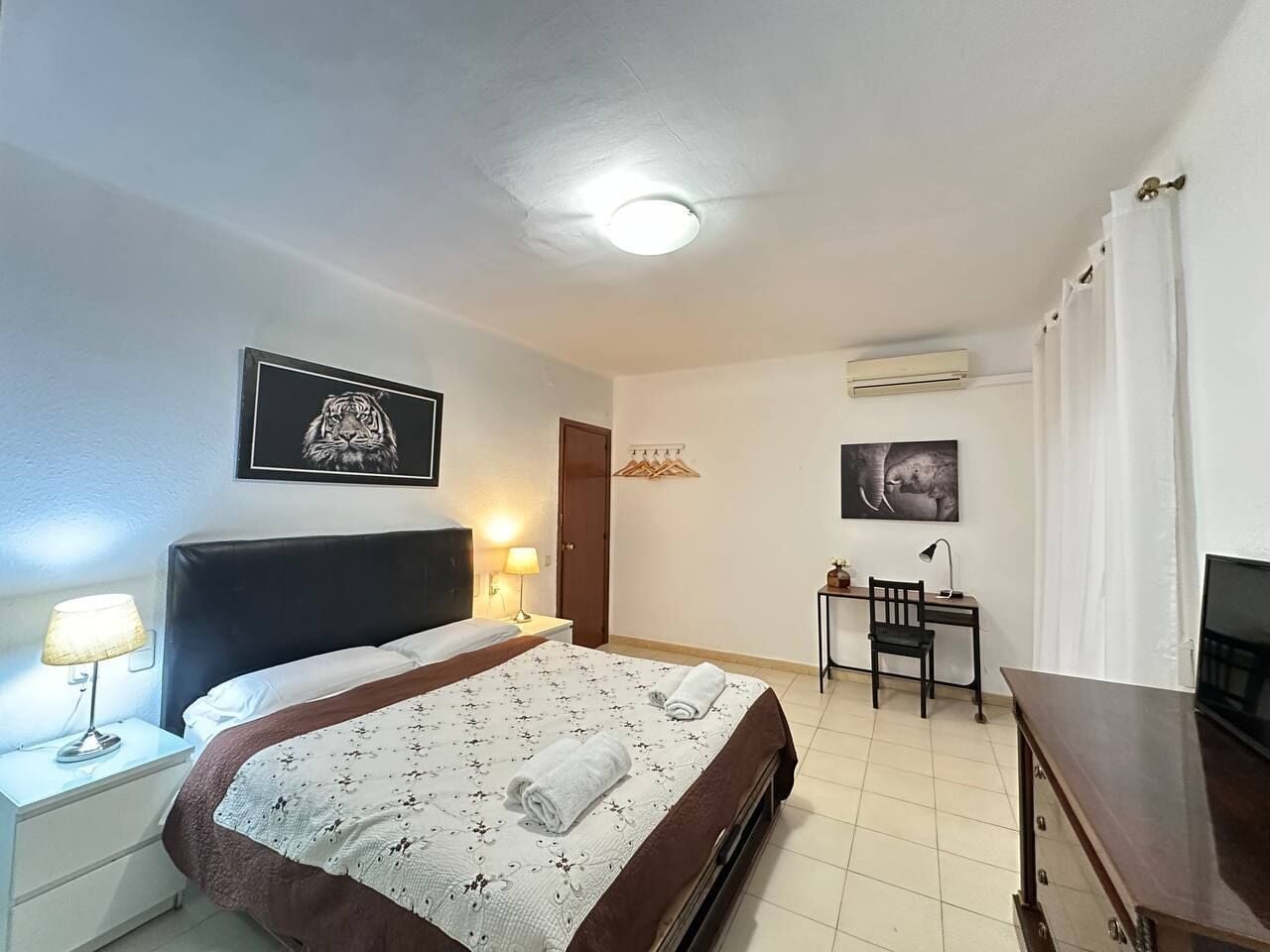 A hotel room with a bed, bedside table, lamp, desk, chair, and a television.