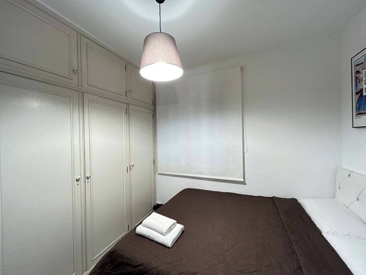 A bedroom with a bed, a wardrobe, a hanging light, and a window.