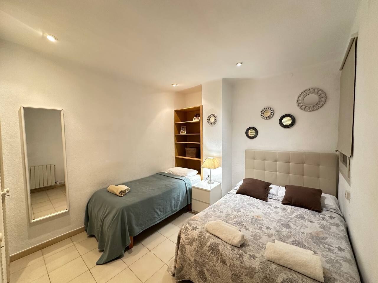 Een slaapkamer met twee bedden, een garderobe, een spiegel en een plank met decoratieve objecten.