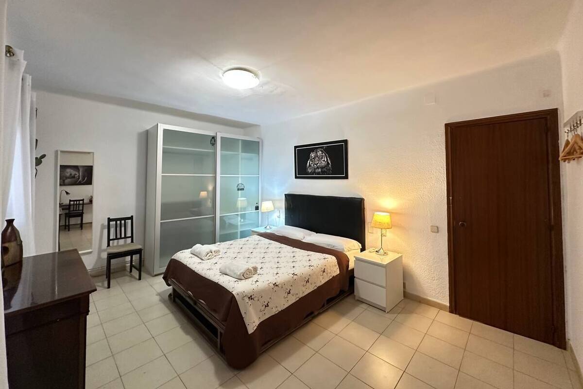 Un dormitorio con cama, mesita de noche, lámpara, armario y una silla.