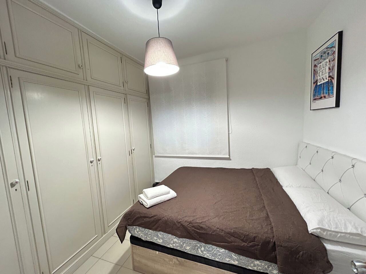 A bedroom with a bed, a wardrobe, a hanging light, and a framed picture on the wall.