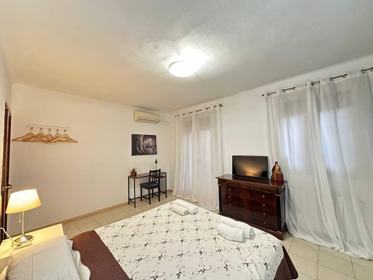A hotel room with a bed, a desk, a chair, a television, and a wardrobe.