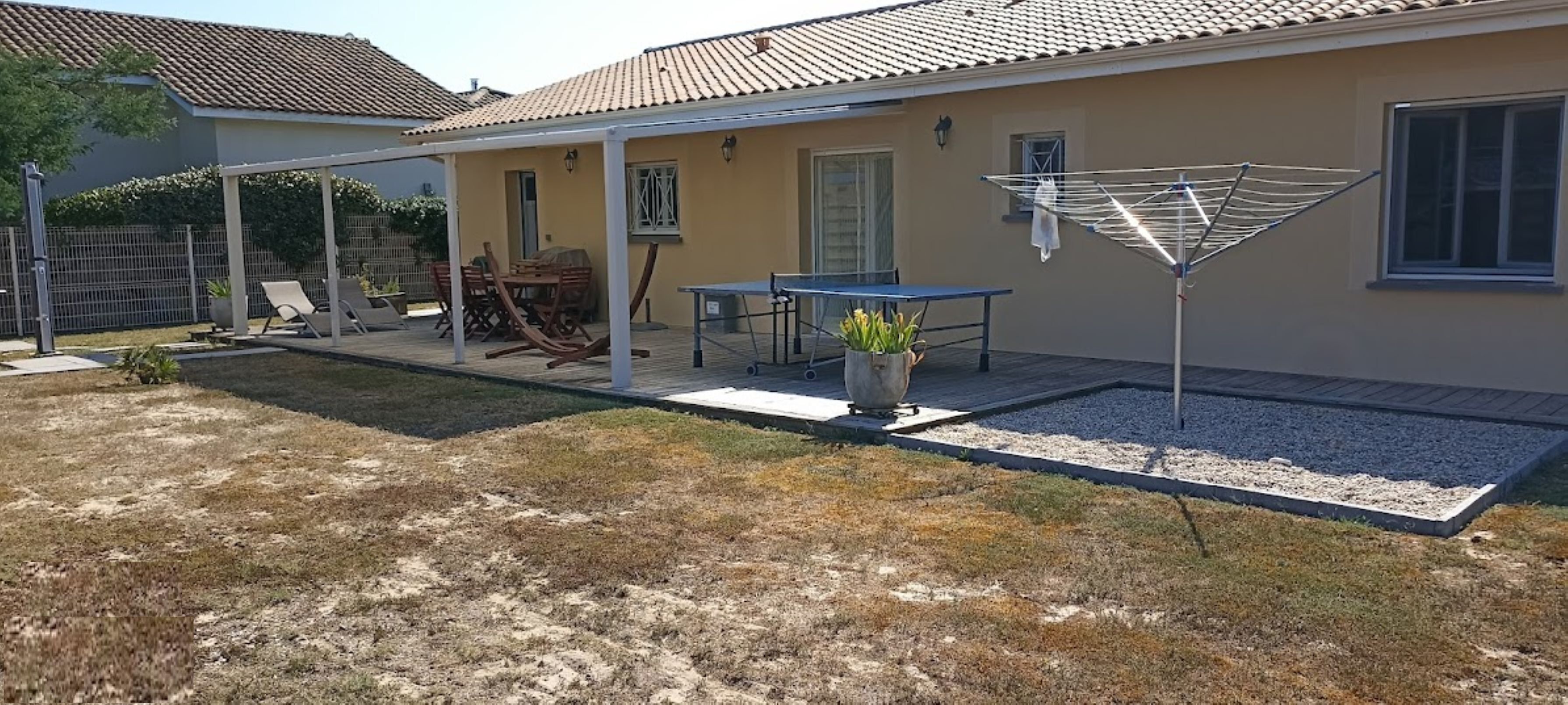 Une maison avec un patio couvert, une table, des chaises et un étendoir.