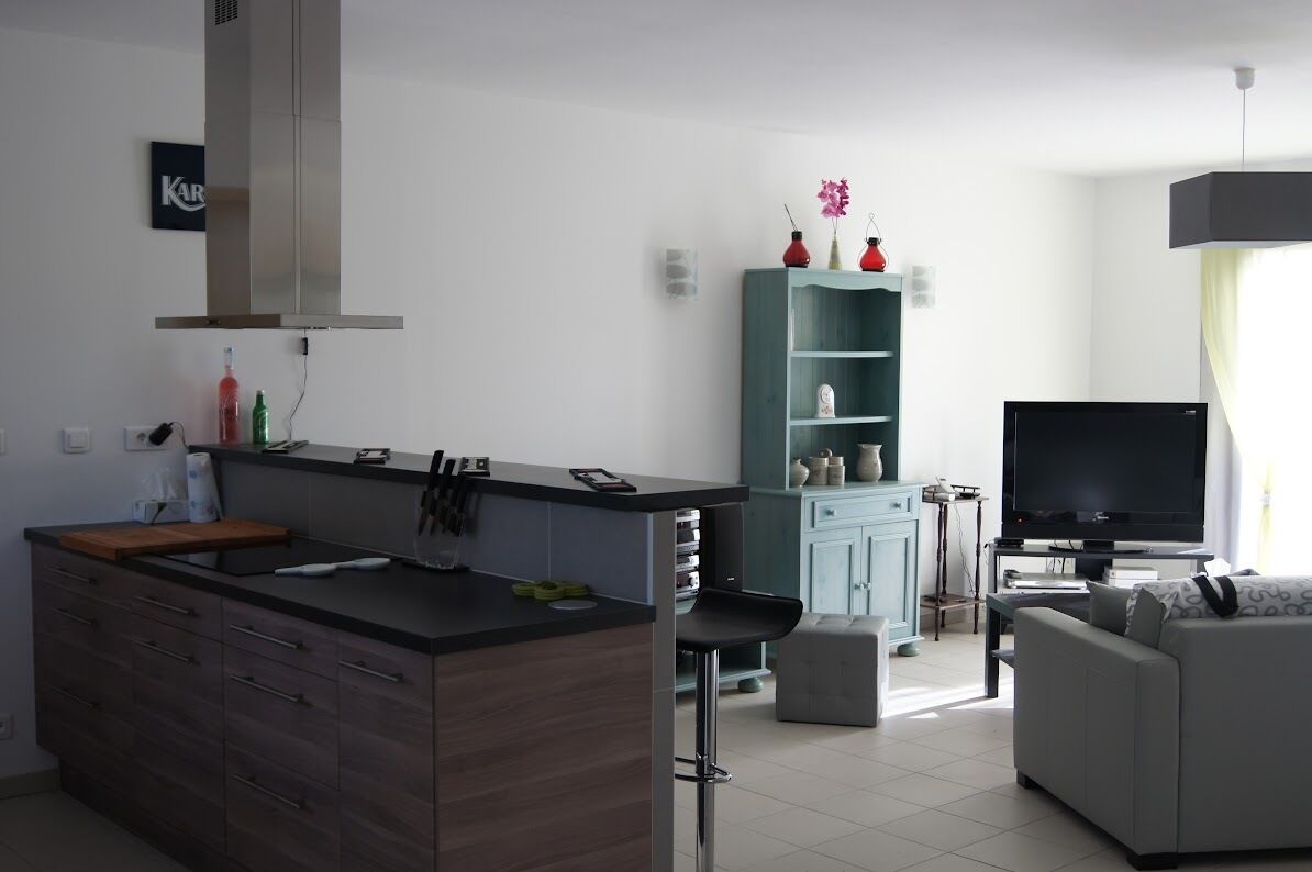 Eine moderne Küche mit Kochinsel, einem Essbereich mit grauem Sofa, einem Fernseher und einem türkisfarbenen Schrank mit Dekoration.