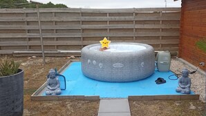 A hot tub with a star decoration, surrounded by a blue mat, with two Buddha statues and a potted plant. - Family home 1000m from the ocean (Vensac)