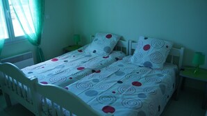 A single bed with a white headboard and footboard, a green bedside table, and a green lamp. - Family home 1000m from the ocean (Vensac)