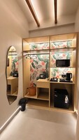 A compact, well-lit room with a mirrored wardrobe, a microwave, a coffee maker, and a small trash bin.