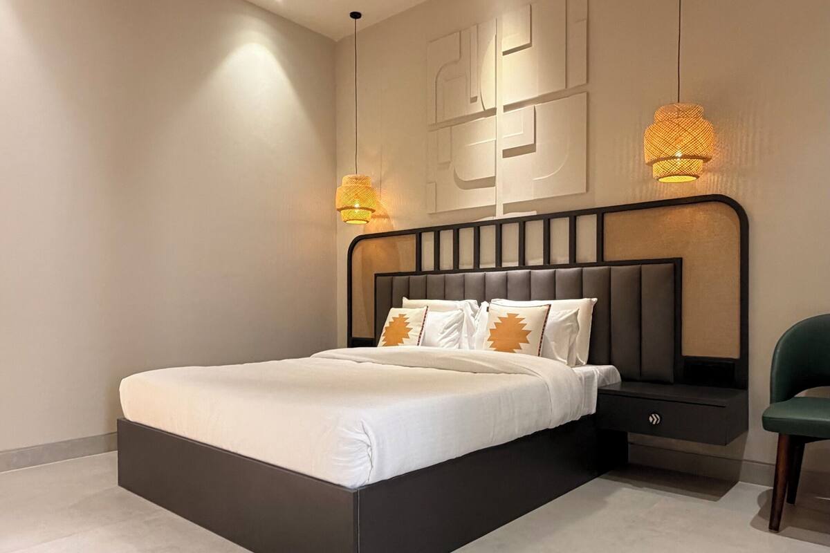 Ein modernes Schlafzimmer mit einem großen Bett, einem Nachttisch, einem Sessel und einer Decke mit freiliegenden Balken und eingelassener Beleuchtung.
