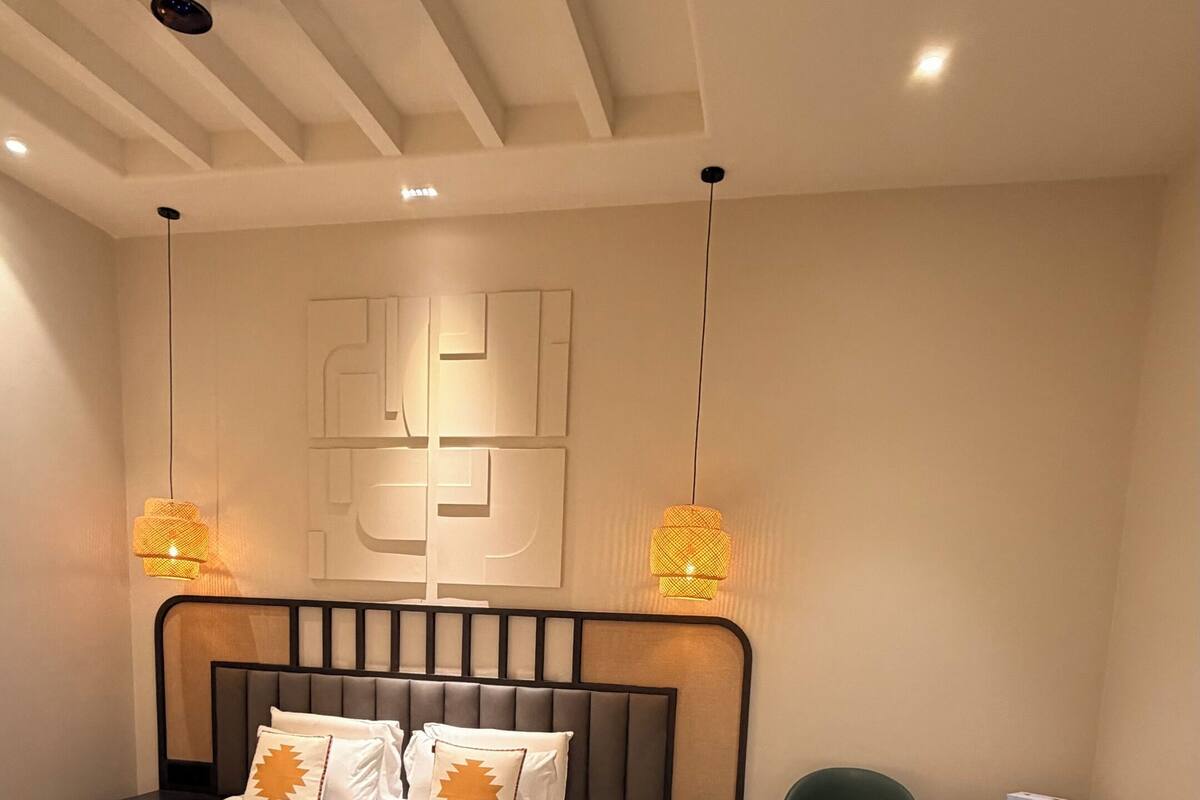 Ein modernes Hotelzimmer mit einem großen Bett, zwei grünen Sesseln, einem kleinen Tisch und Pendelleuchten.