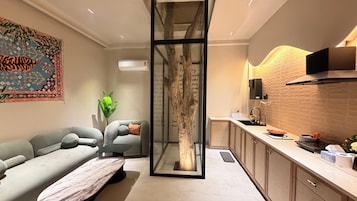 A modern living room with a sofa, a glass partition, and a kitchen area with a sink and cabinets.