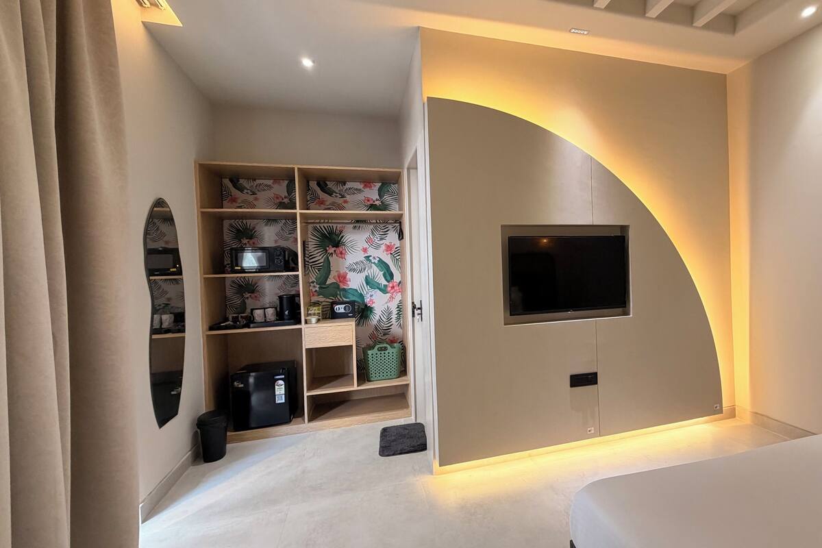 Ein modernes Hotelzimmer mit integriertem Fernseher, einer gemütlichen Sitzecke und einer kleinen Küchenzeile.