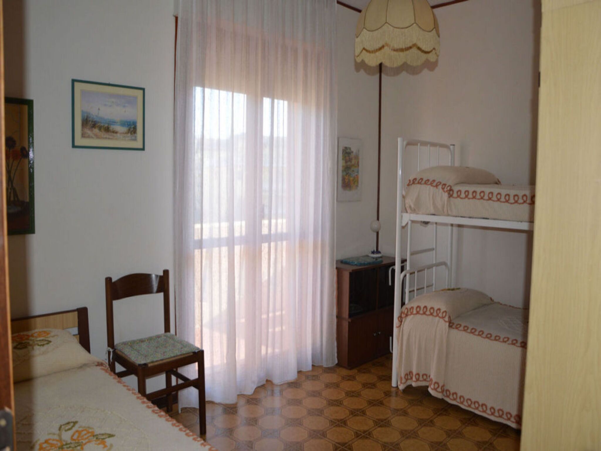 Ein Zimmer mit einem Etagenbett, einem Sessel, einem Schreibtisch, einer Lampe und einem Fenster mit Vorhängen.