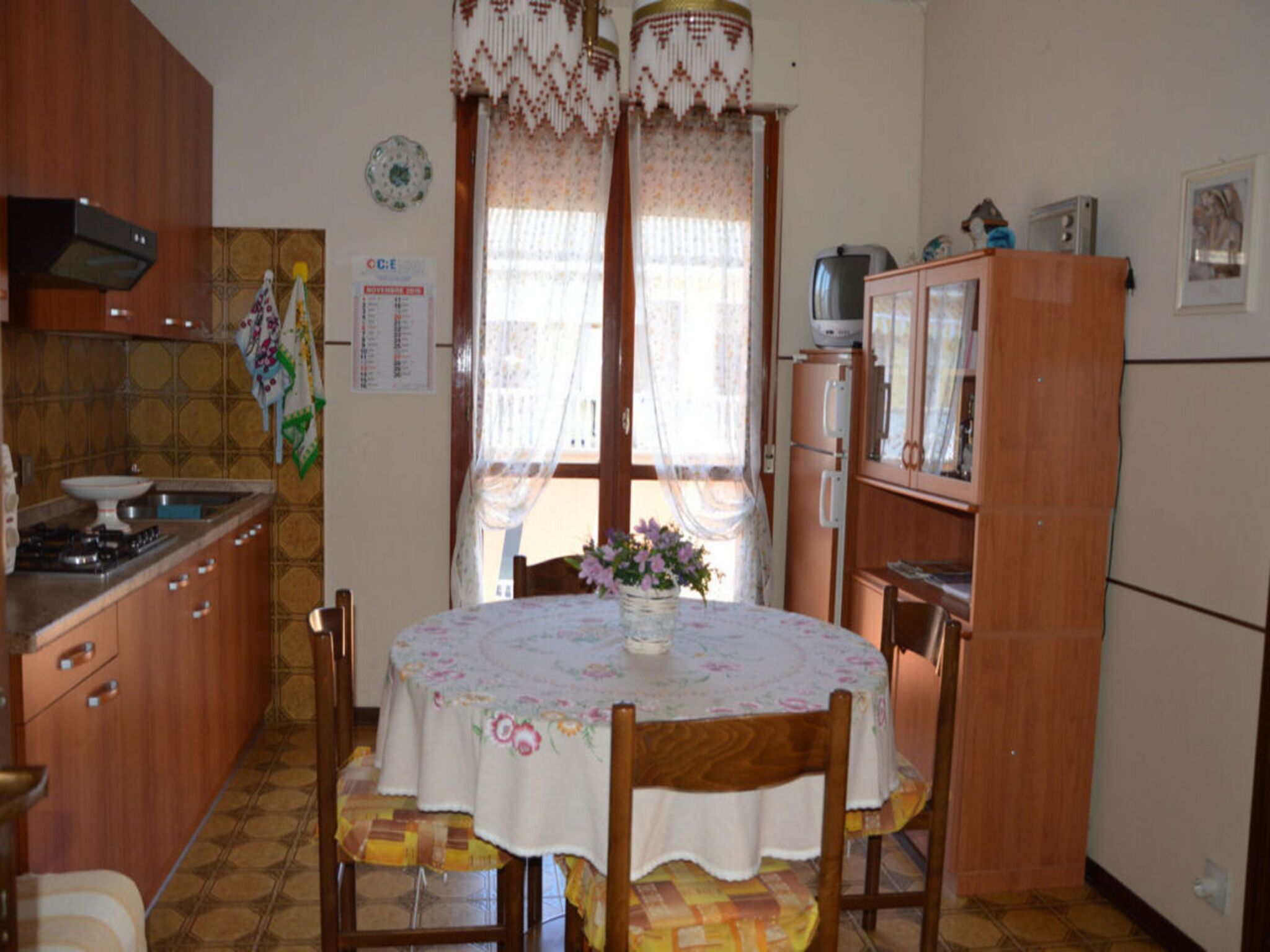 Cucina compatta con mobili in legno, piano cottura a gas, frigorifero e tavolo con sedie.