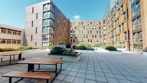 Une cour avec des espaces de repos en plein air et un bâtiment moderne à plusieurs étages doté de grandes fenêtres.