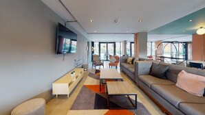 Un salon moderne avec un canapé, une table basse et des fauteuils. Un téléviseur à écran plat est fixé au mur.