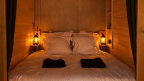 A cozy wooden cabin-style bedroom with a bed, two bedside lamps, and a headboard. - Unusual accommodation with jacuzzi and paddle (Mostuéjouls)
