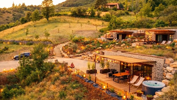A rustic outdoor patio area with stone walls, wooden deck, and seating. - Unusual accommodation with jacuzzi and paddle (Mostuéjouls)
