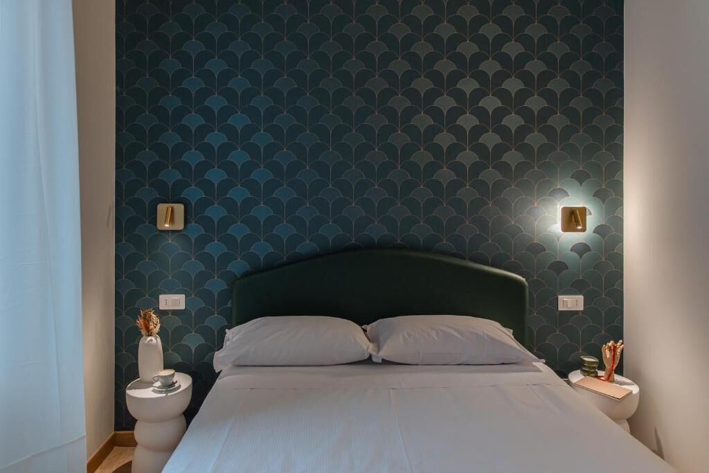 Una cama bien hecha con sábanas blancas, un cabecero tapizado en verde oscuro y una pared con diseño geométrico.