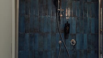 Une salle de bain avec un mur de douche recouvert de carreaux bleus, une douchette à main et un robinet fixé au mur.