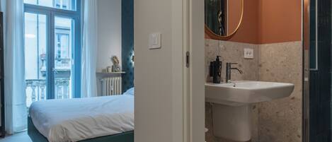 A bedroom with a bed, a window, and a bathroom with a sink and mirror.