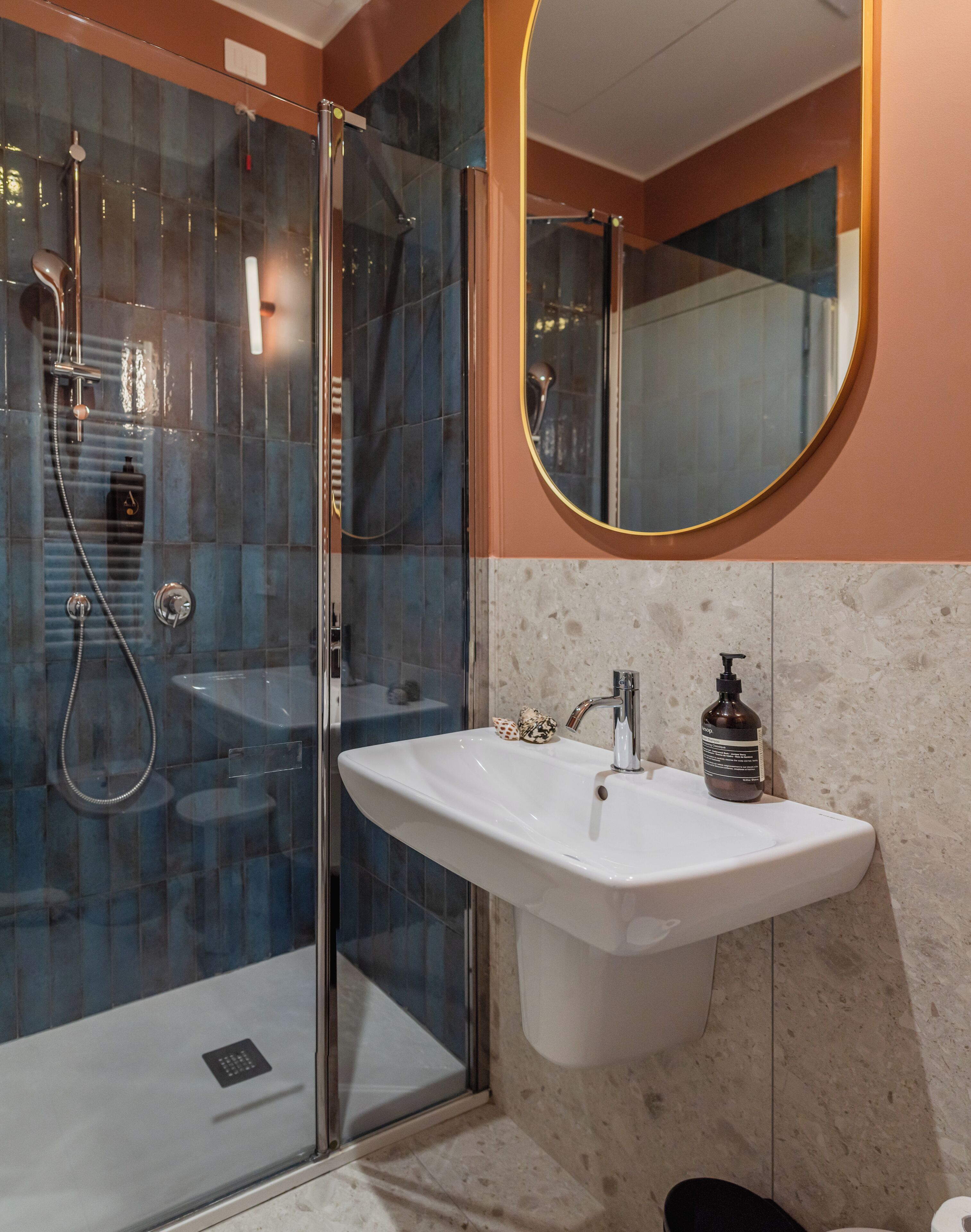 Un baño moderno con ducha envuelta en vidrio, un lavamanos blanco con dispensador de jabón y un espejo redondo.