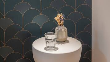 A bathroom with a round pedestal sink, a vase with flowers, and a glass of water on the sink.