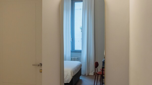 Una habitación con cama, una silla, una mesita, un espejo y un inodoro.