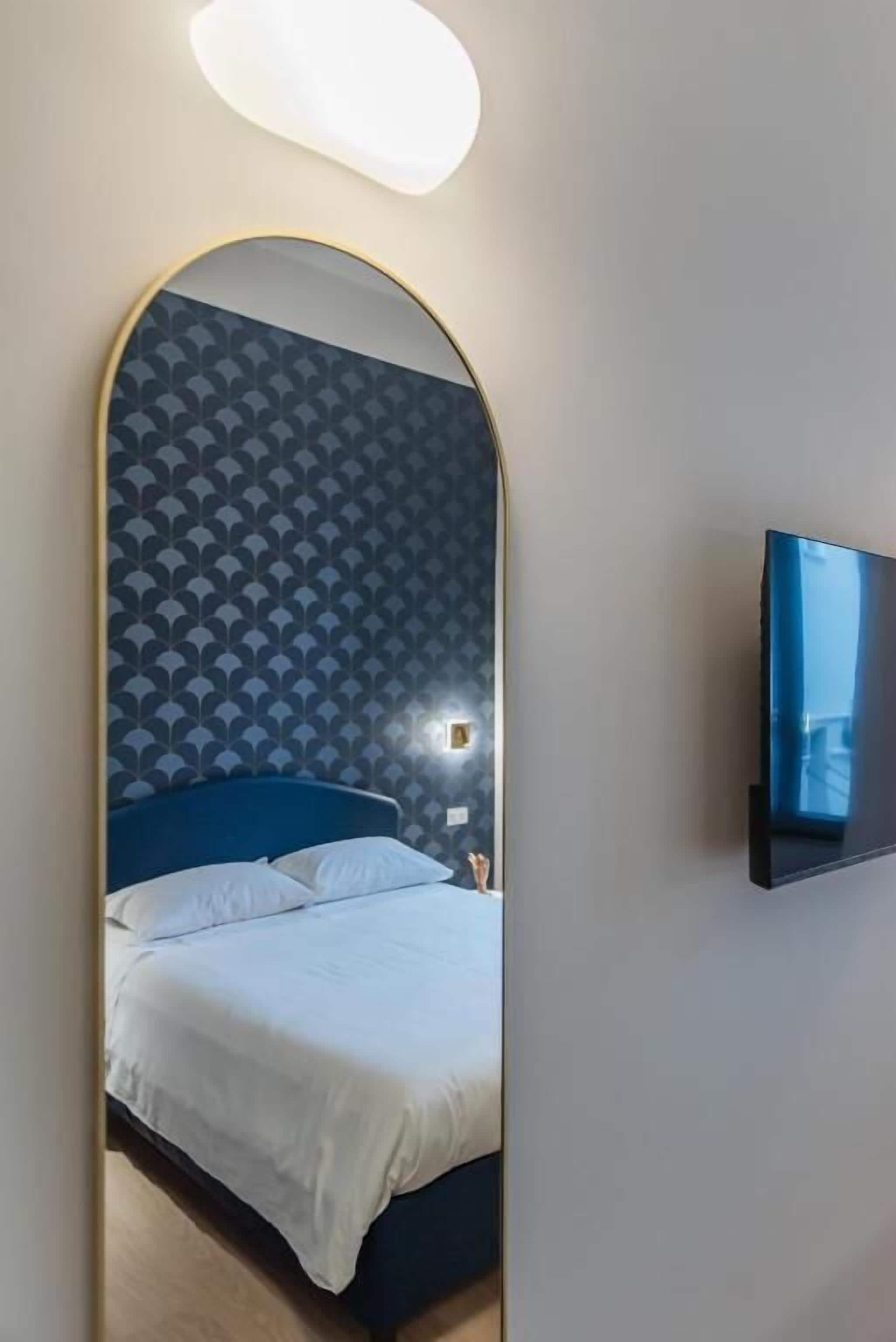 A hotel room with a bed, a TV mounted on the wall, and a mirror reflecting the room.