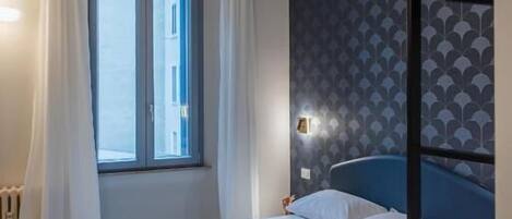A bedroom with a bed, a window with curtains, a wall with a geometric pattern, and a radiator.