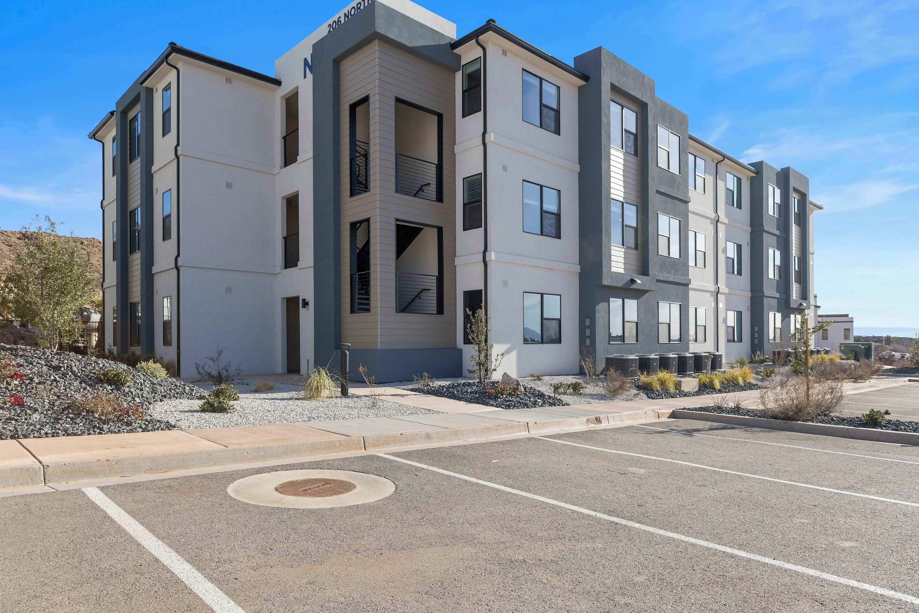 A multi-story residential building with a modern architectural design, featuring balconies and a parking lot in front.