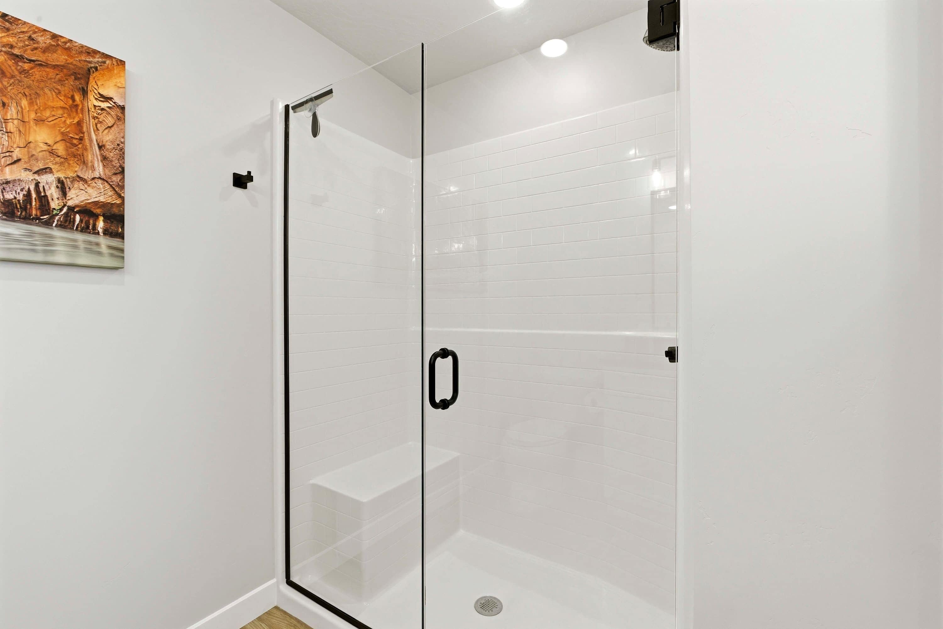 Une douche fermée par des parois en verre, avec des murs recouverts de carreaux blancs et une poignée de porte noire.