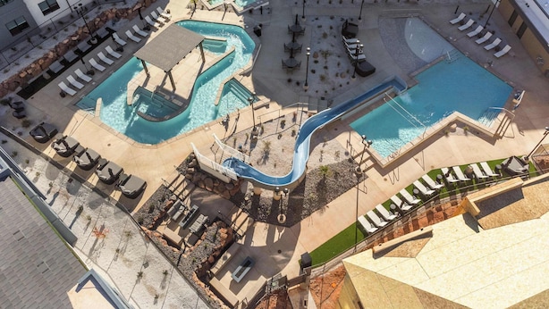 Vista aérea de un hotel con múltiples piscinas, incluyendo un tobogán acuático, zonas de descanso y mobiliario exterior.