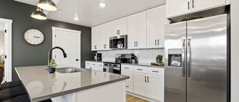 A modern kitchen with white cabinets, stainless steel appliances, and a central island.