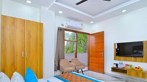 Un dormitorio con cama, televisor, armario, ventana con cortinas y balcón con sillas.