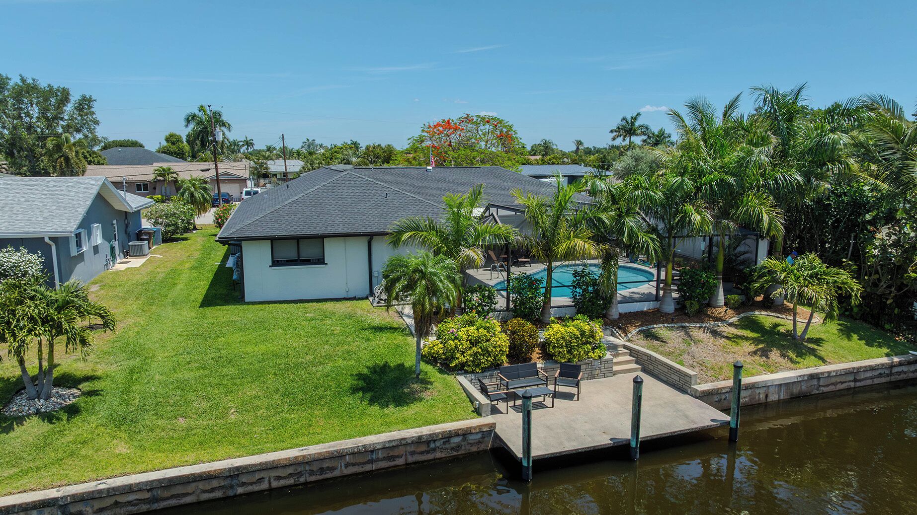 A residential property with a swimming pool, a grassy yard, and a dock extending into a body of water.