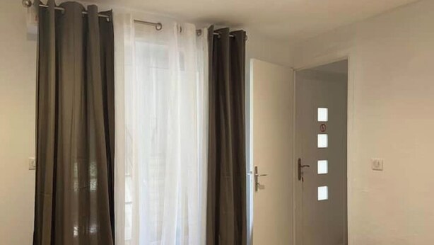Ein Zimmer mit einem Bett, einer Tür mit Fenster und Vorhängen.