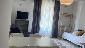 Ein modernes Hotelzimmer mit Esstisch, Fernseher, Bett und einem Fenster mit Vorhängen.