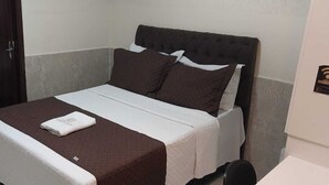 A single bed with a dark headboard and two pillows, a white blanket, and a folded white towel on the bed.