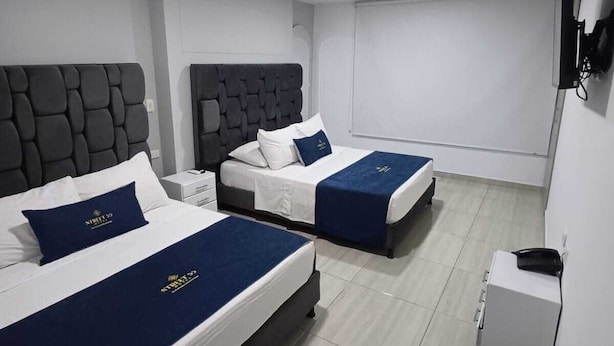 Une chambre d’hôtel avec deux lits, chacun doté d’une tête de lit, de draps blancs et de coussins décoratifs bleus. On y trouve une petite table de chevet avec une lampe et un téléphone.