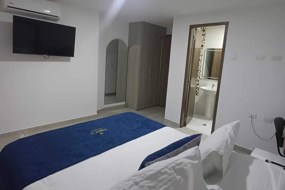 Ein Hotelzimmer mit Bett, einem an der Wand befestigten Flachbildfernseher, einem Schrank und einem durchgehenden Türspalte sichtbaren Badezimmer.