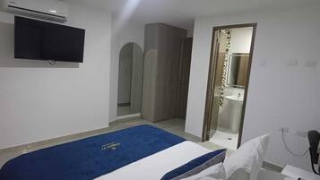 Una camera d'albergo con un letto, una TV a schermo piatto montata a parete, un armadio e un bagno visibile attraverso una porta aperta.
