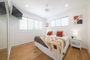 Ein Schlafzimmer mit einem Bett, Nachttischen, einem Deckenventilator und Fenstern mit Jalousien.