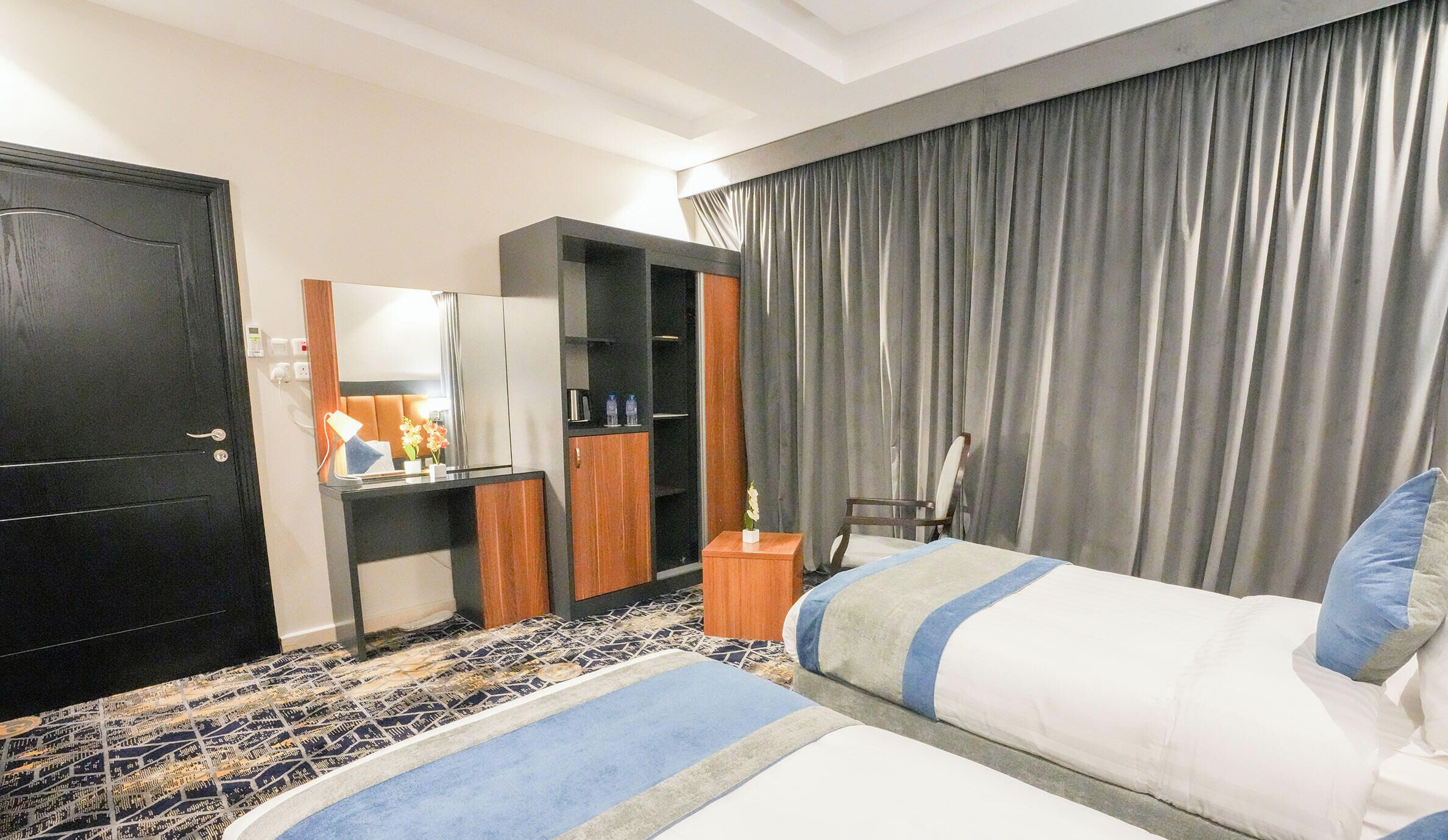 Una habitación de hotel con cama, escritorio, armario y un amplio ventanal con cortinas.
