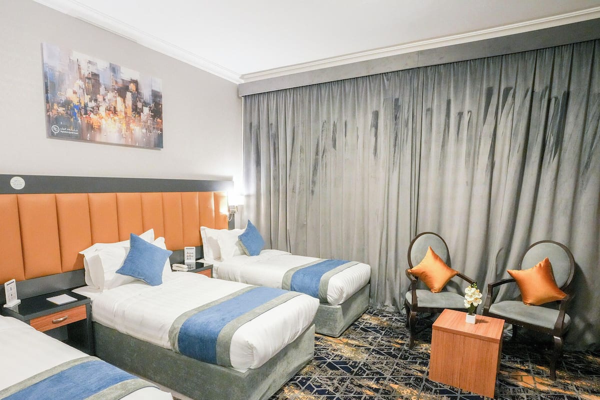 Habitación de hotel con dos camas, un escritorio, una silla y un ventanal con cortinas.